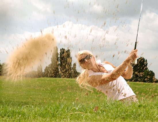 A woman golfer hitting ball out of sand trap